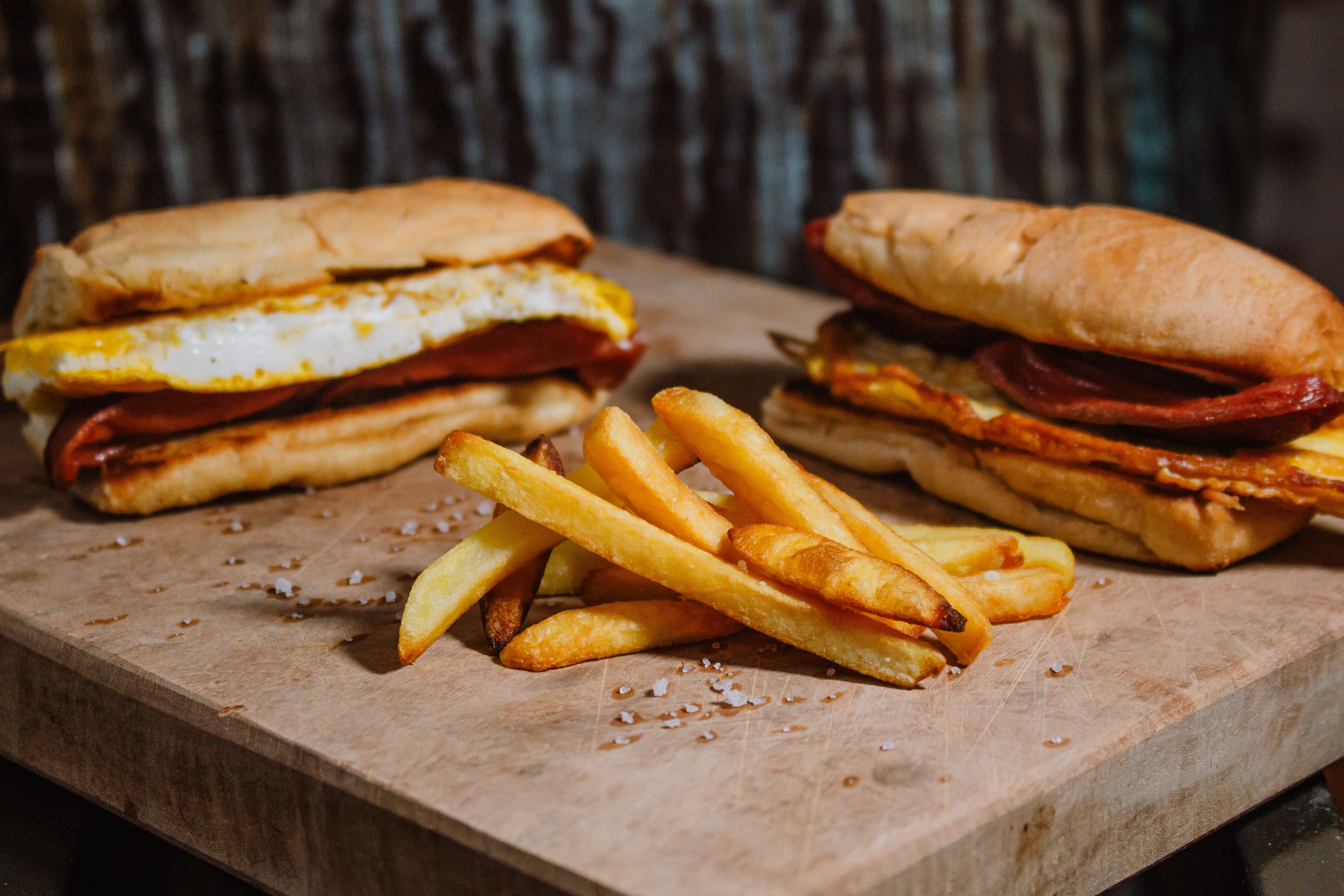 Close-up of two sandwiches with fried eggs and french fries on a wooden board, perfect for lunch.